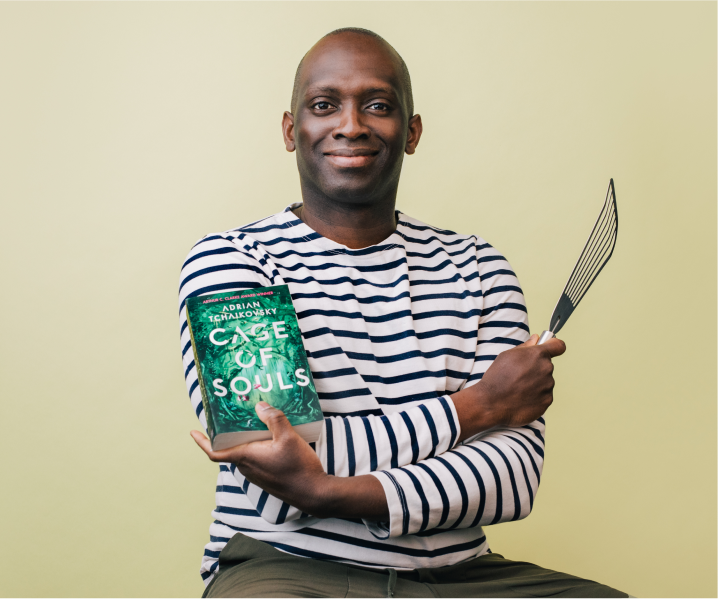 Ayo holding cooking utensils and the book 'Cage of Souls'